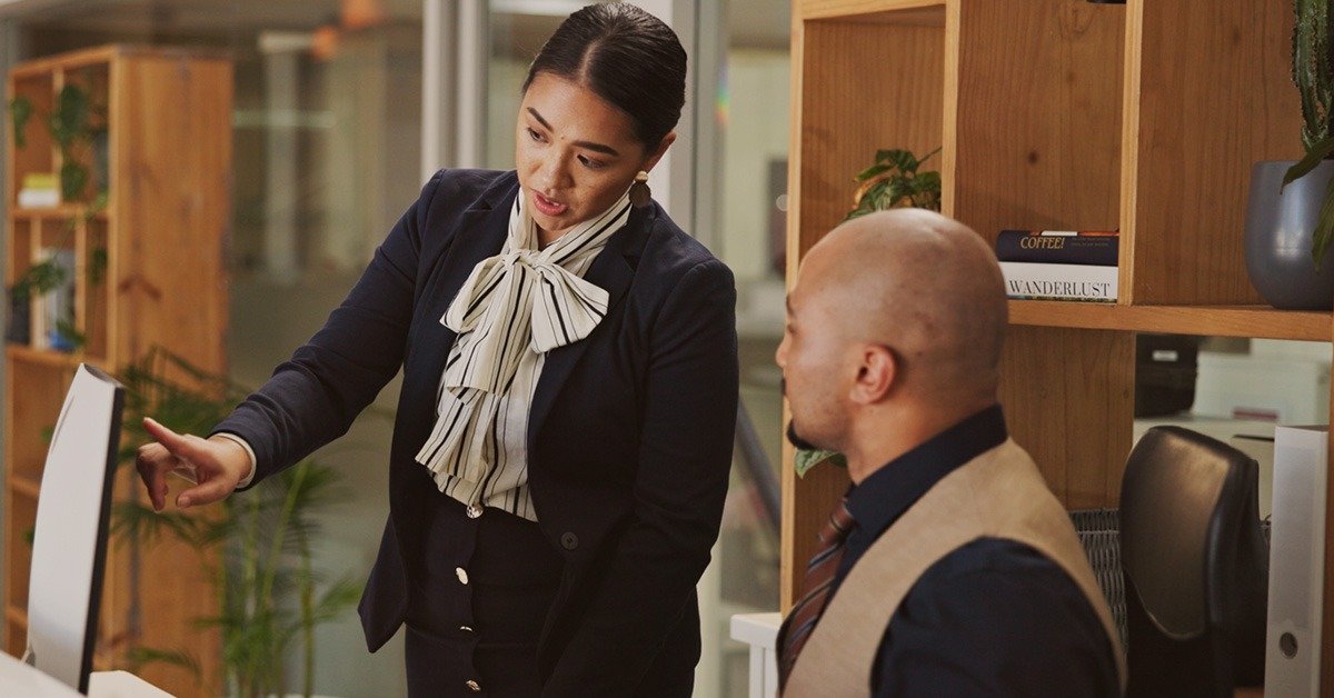 Small hotel manager discussing pricing with areceptionist in front of the computer. Illustration for guide on dynamic pricing for small hotels, inns, and b&bs.